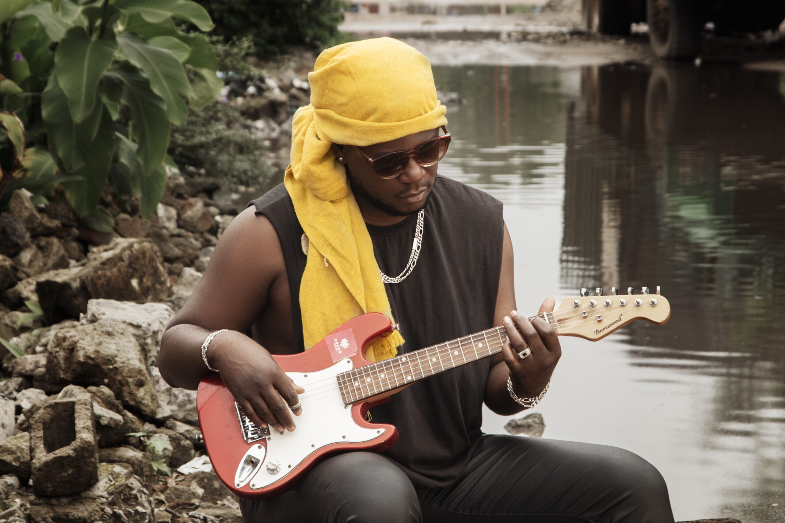 artiste de face jouant de la guitare électrique, un foulard jaune sur la tête avec des lunettes de soleil